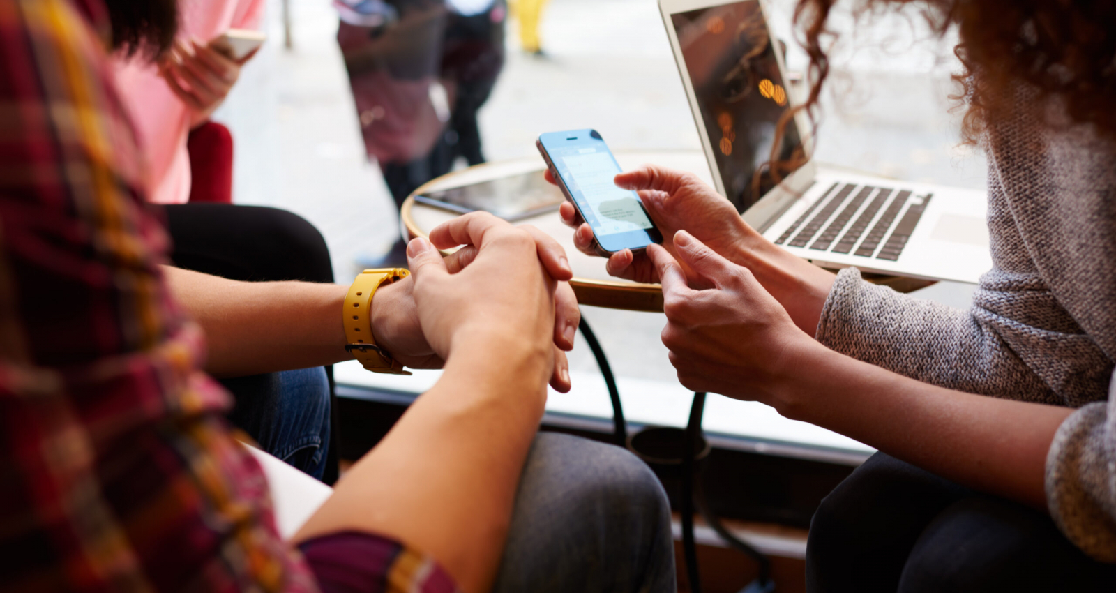 Closely image of woman is making an on-line purchase via cell telephone, while is sitting with friends in hipster cafe interior. Young female is reading information on web page via her mobile phone